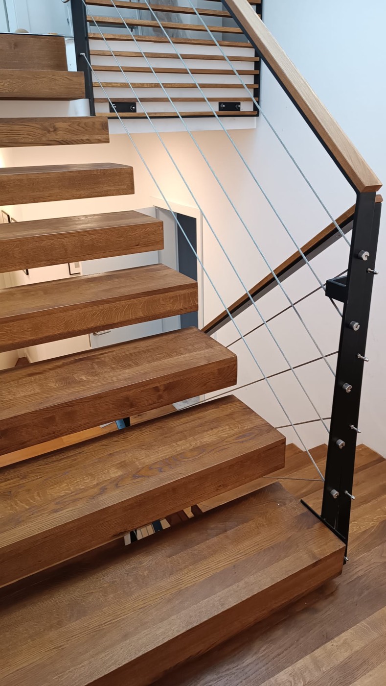 Freitragende Treppe aus Eichenholz mit schwarzem Geländer und Seilbespannung